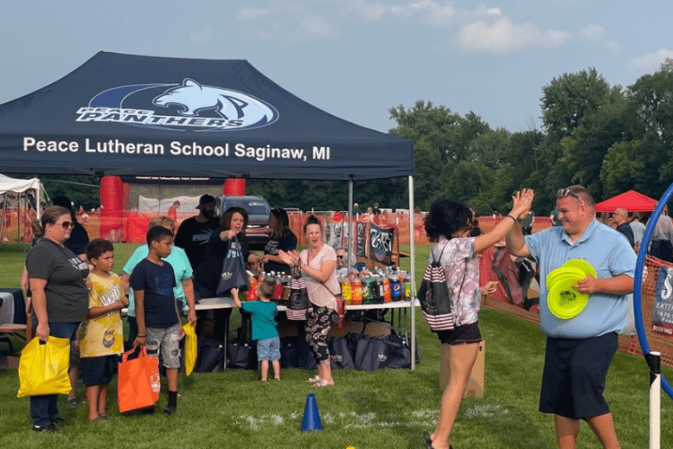 A Peace Lutheran School gazebo is set up at an event with children and families gathered around.
